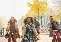 Усміхнені молоді друзі катаються на велосипеді на міській осінній вулиці — стокове фото