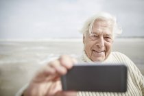 Усміхнений старший чоловік бере селфі з мобільним телефоном на пляжі — стокове фото