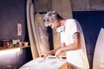 Surfboard designer taping surf board in workshop — Photo de stock