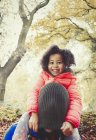 Retrato sonriente hija tirando de media gorra sobre la cabeza de los padres en otoño parque - foto de stock