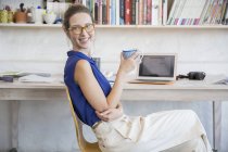 Молода жінка сидить з чашкою в домашньому офісі — стокове фото