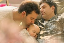 Affectionate male gay parents kissing sleeping baby son — Stock Photo