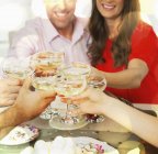 Улыбающаяся пара пьет бокалы шампанского с друзьями за столом — стоковое фото