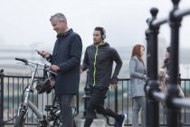 Businessman with bicycle texting with cell phone and male runner on urban ramp — Stock Photo