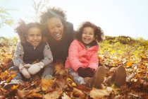 Porträt verspielte Mutter und Töchter im Herbstlaub im sonnigen Park — Stockfoto