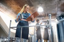 Female coffee roaster looking down at clipboard near tank — Stock Photo