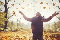 Verspieltes Mädchen wirft Herbstblätter über Kopf in sonnigem Park — Stockfoto
