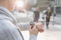 Corredor femenino comprobando reloj inteligente en calle urbana - foto de stock