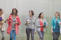 Mulheres sorridentes andando com tapetes de ioga e café — Fotografia de Stock