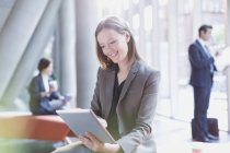 Lächelnde Geschäftsfrau mit digitalem Tablet in sonniger Büro-Lobby — Stockfoto