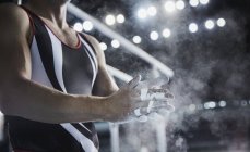 Hombre gimnasta frotando tiza en polvo en las manos por debajo de las barras paralelas - foto de stock