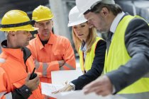Ingenieros y trabajadores de la construcción revisando planos en el sitio de construcción - foto de stock