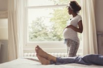 Nachdenkliche Schwangere schaut aus Schlafzimmerfenster — Stockfoto