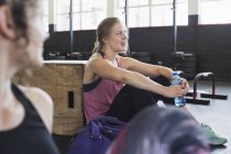 Mujer joven sonriente descansando y bebiendo agua después del entrenamiento en el gimnasio - foto de stock
