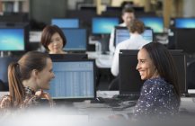 Улыбающиеся деловые женщины, разговаривающие за компьютерами в офисе открытого плана — стоковое фото