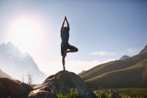 Young man balancing in tree pose on rock in sunny, remote valley — Stock Photo