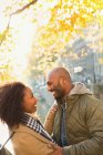 Lächelndes, liebevolles junges Paar, das sich unter dem sonnigen Herbstbaum umarmt — Stockfoto