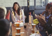 Друзі плескають за щасливу жінку з феєрверком на день народження торт за столом ресторану — стокове фото