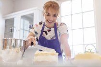 Усміхнена жінка випічка, глазурований шар торта на кухні — стокове фото