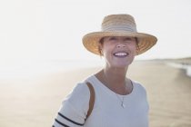 Portrait smiling mature woman wearing straw hat on sunny summer beach — Stock Photo