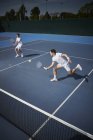 Joven tenista masculino dobla jugadores jugando al tenis, alcanzando la pelota en la soleada cancha de tenis azul - foto de stock