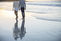 Пара держащихся за руки и гуляющих по пляжу — стоковое фото