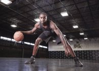 Portrait confident young male basketball player dribbling the ball on court in gymnasium — Stock Photo