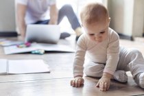 Baby daughter sitting on floor near father working at laptop — Stock Photo
