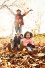 Mãe brincalhão e filhas jogando folhas de outono no parque ensolarado — Fotografia de Stock
