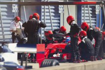 Pit crew replacing tires on formula one race car in pit lane — Stock Photo
