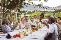 Jovem casal e seus convidados sentados à mesa durante a recepção do casamento no jardim — Fotografia de Stock