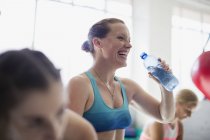 Mujer riéndose bebiendo agua y descansando después del entrenamiento en el gimnasio - foto de stock