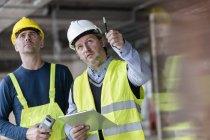 Polier und Ingenieur mit Klemmbrett schauen auf Baustelle hoch — Stockfoto
