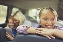 Smiling girl listening to music with headphones in back seat of car — Stock Photo