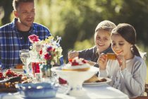 Батько спостерігає за дочками, які їдять на сонячній вечірці в саду — стокове фото