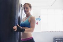 Retrato confiante, difícil boxeador feminino em saco de perfuração no ginásio — Fotografia de Stock