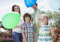 Young girl holding bunch of balloons, family standing behind her — Stock Photo