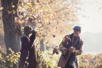 Couple sénior ludique jetant des feuilles d'automne dans un parc ensoleillé — Photo de stock