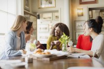 Smiling women drinking coffee and talking at restaurant table — Stock Photo