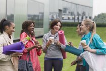 Жінки друзі з килимками для йоги та кавою розмовляють поза спортзалом — стокове фото
