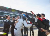 Piloto de Fórmula 1 e equipe de corrida comemorando a vitória na pista de esportes — Fotografia de Stock