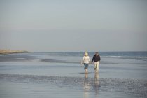 Зріла пара тримає руки, ходячи в сонячному океані пляжний серфінг — стокове фото