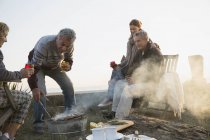 Mature couples barbecuing and drinking wine on sunset beach — Stock Photo