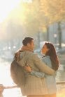 Smiling young couple hugging on sunny autumn bridge over canal — Stock Photo