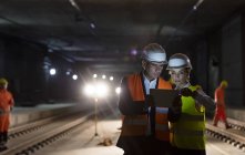 Contremaître et travailleur de la construction utilisant une tablette numérique sur un chantier souterrain sombre — Photo de stock