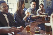 Друзі п'ють пиво і вино і розмовляють за столом у барі — стокове фото