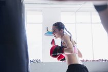 Determinado jovem boxeador do sexo feminino boxe no saco de perfuração no ginásio — Fotografia de Stock
