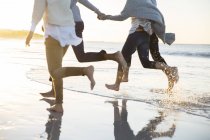 Група з чотирьох друзів тримає руки і бігає на пляжі — стокове фото
