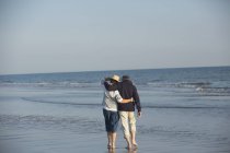 Affectueux couple d'âge mûr câlin, marche dans l'océan ensoleillé plage surf — Photo de stock