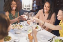 Sorridente donne amiche brindare bicchieri di vino bianco pranzo al tavolo del ristorante — Foto stock